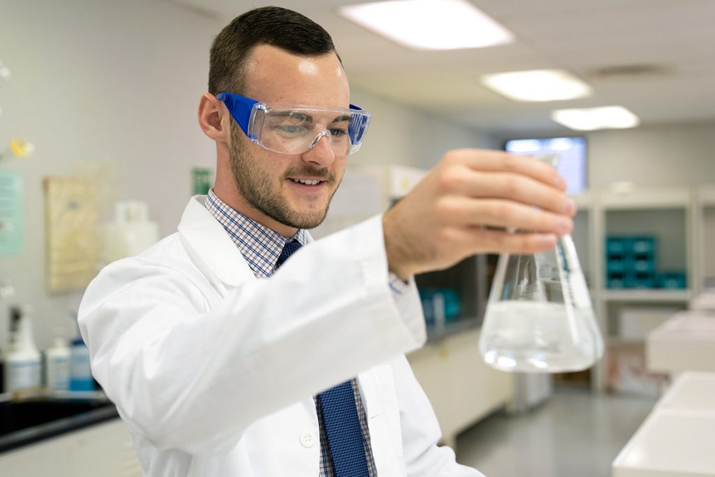 derek donaldson in goggles holding a beaker in a pharmacy lab